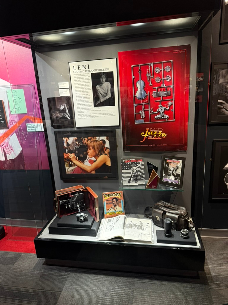 Display case with Leni Sinclair exhibition materials, cameras, programs, and archival objects